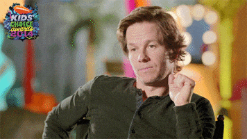 Celebrity gif. Mark Wahlberg sits a bit slouched in his chair. He has a bored expression on his face and then he shrugs with a simple hand gesture, and smirks sassily.