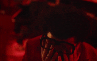 Music video gif. We see The Weeknd in Heartless with his hands over his face, under his glasses, awash in red light as he moves up in frame. 