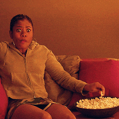 Celebrity gif. Regina Hall sits riveted near a bowl of popcorn on a couch. Her gaze focused ahead as she eats a handful of popcorn.