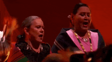 Oscars 2024 gif. Scott George and Osage singers perform 'Wahzhazhe (A Song For My People)' from Killers of the Flower Moon. Two women swathed in Indigenous dance shawls sing passionately. 