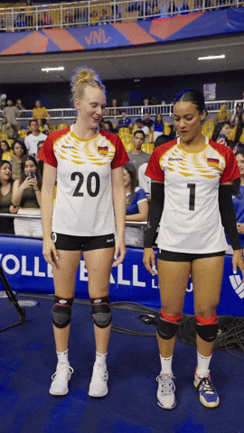 Video gif. Two German volleyball players, Emilia Weske and Vanessa Agbortabi do a peppy coordinated dance move on the sidelines of a match.