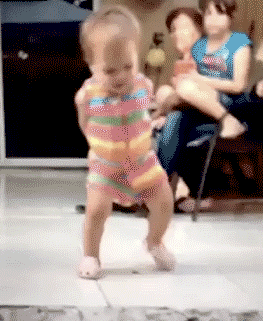 Video gif. Footage of a baby in a striped onesie, walking awkwardly with their hands behind their back. They shift their weight into a cheerful and much more coordinated dance.