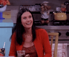Friends gif. Courteney Cox as Monica sits at her kitchen table wearing a red cardigan. She gives an exaggerated smile to someone, then tilts her head to the side playfully tell them: Text, "No."