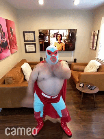 Video gif. Phone video of a man dressed in a Nacho Libre costume dances in his living room for us, his arms windmilling around.