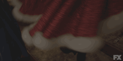 TV gif. MJ Rodriguez as Blanca from Pose spins around in front of a mirror, trying out a Christmassy red coat with sequins and white fur lining.