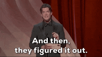 Oscars 2024 gif. John Mulaney wears a full black suit onstage. He shakes his head while saying, "And then, they figured it out."