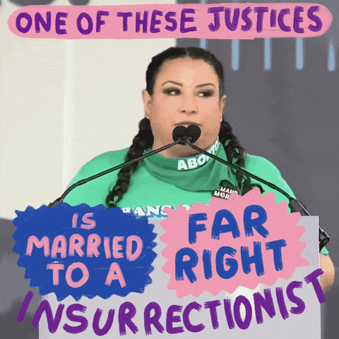 Video gif. Woman wearing a bright green t-shirt speaks emphatically at a podium above a sign that reads, "Bans off our bodies." She says, "One of these justices is married to a far right insurrectionist."
