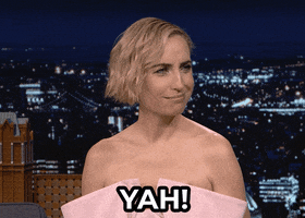Celebrity gif. Wearing a strapless pink dress, Zoe Lister-Jones on the Tonight Show looks around and laughs. At a slight loss for words, she says: Text, "Yah!"