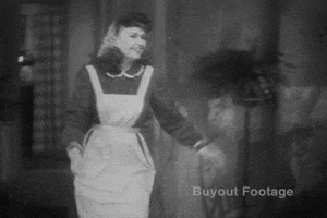 Video gif. Black and white footage of a woman wearing an apron running toward a man in a suit before they embrace each other with a kiss.