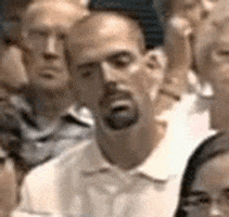 Video gif. A man in a crowd of people furrows his eyes in confusion and then shakes his head as if he can't believe what he just heard.