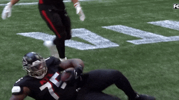 Sports gif. Kentavius Street of the Atlanta Falcons poses on his side on the football field with a hand behind his head and the other holding and intercepted football. Another player runs up and slaps him excitedly on the stomach and leg. 