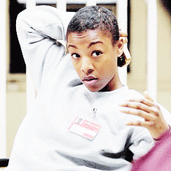 TV gif. Samira Wiley as Poussey in Orange is the New Black brushes the back of her cropped hair and looks up as an amused smirk emerges on her face.