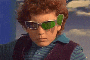 Movie gif. Daryl Sabara as Juni in Spy Kids moves toward us as a cascade of green lenses emerge from his sunglasses.