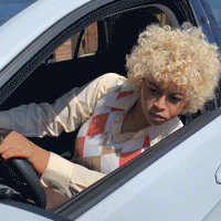 Celebrity gif. Fia Oruene leans her head out of the car she’s driving. She’s parallel parked and is stuck super close in between two cars so she edges back and stops. She cringes and then edges forward, but stops. She then closes her eyes  and turns her wheel really quickly, perfectly making it out of the spot. She pulls up to us, looking up with a big grin and a thumbs up. Text, “Coming out is hard but worth it.”
