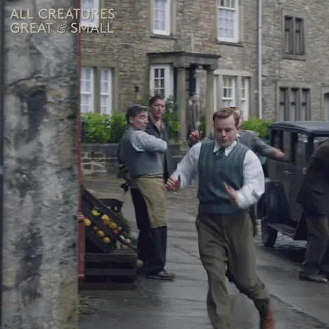 TV gif. Callum Woodhouse as Tristan on All Creatures Great and Small running around the corner of a stone building with a friend.