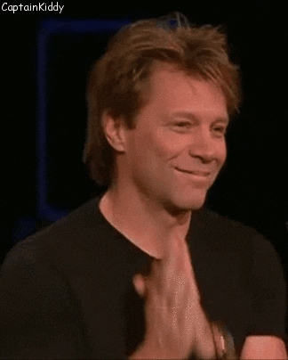 Celebrity gif. Bon Jovi smiles as he leans his head endearingly on his folded hands.