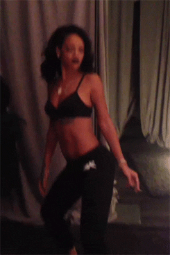 Celebrity gif. Rihanna wears a black bikini top and a pair of black sweats as she twerks and tosses her head seductively.