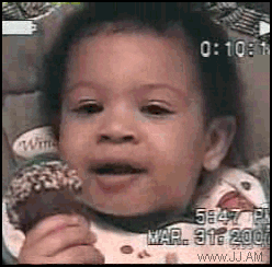 Video gif. Home video of a baby wearing a bib and holding a drumstick ice cream cone, smiling and beginning to laugh, but then suddenly frowning, confused.