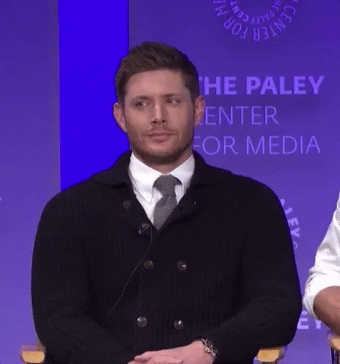 Celebrity gif. Jensen Ackles as Dean in Supernatural is at a conference and he looks confused and uncomfortable as he listens. He cocks his head and puts one finger up before looking around at his castmates as he begins to asks for clarification.