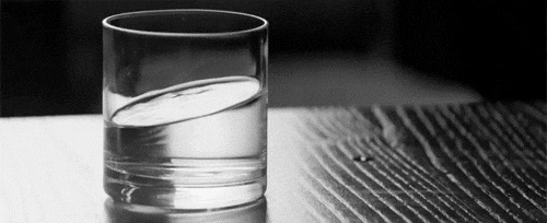 A glass of water on a black wooden surface, shaking slightly, with the water sitting at an angle.