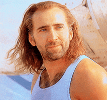 Movie gif. Nicolas Cage as Cameron in Con Air. His long hair is billowing in the wind and we zoom in as he sends us a wink.