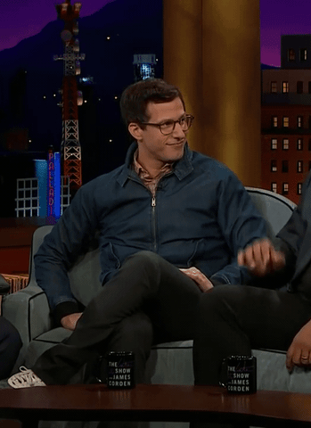 Celebrity gif. Actor Andy Sandberg sits in a chair during an interview. He slaps his hands together in a burst of excitement and shouts, “Boom!” The text, “boom” appears like an explosion as well.