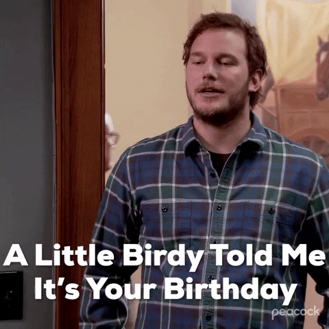 Parks and Recreation gif. Chris Pratt as Andy is standing in a doorway with his hands on his hips, looking down at someone sitting. He has a sly smile on his face and he says, "A little birdy told me it's your birthday."