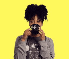 Video gif. Woman holding a mug of tea to her face blinks flirtatiously in front of a yellow background.