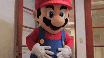 Video game gif. A life sized Mario walks into a room and waves at us.
