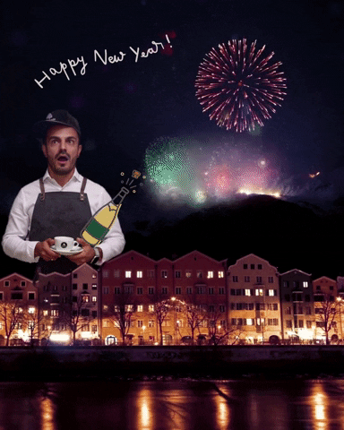 Video gif. A man standing above the scene of a neighborhood at night holds a cup of coffee, his jaw dropped in amazement while fireworks explode above the mountaintops behind him. In the crook of his arm is a champagne icon with the cork popping. Above him reads the message, “Happy New Year!”