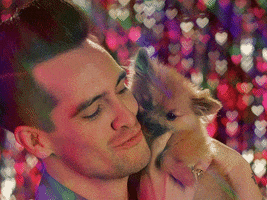 Celebrity gif. Brendon Urie is holding a puppy close to his face and he coos at it.
