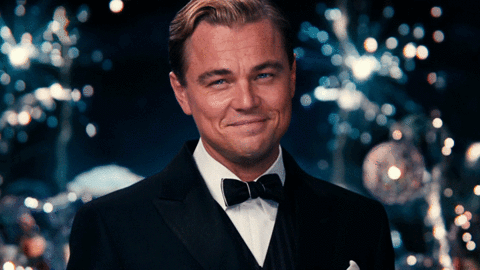 GIF showing The Great Gatsby raising a Martini Glass with Fireworks behind him.