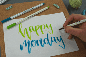 Video gif. We look down at a piece of paper with hand-drawn green and blue script that reads, "Happy Monday." A person outside our view draws a green heart to the side.