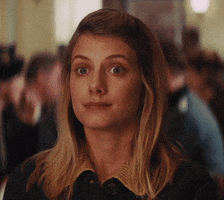 Movie gif. Mélanie Laurent as Shoshanna in Inglorious Basterds. She sits awkwardly at a table and her body is tense. Her eyes dart up and back and she does a half smile while giving a tight nod.