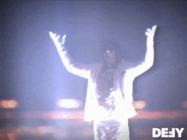Reality TV gif. Criss Angel from Mindfreak hovers high above a glowing skyscraper with his hands raised. Text, "Yeah."