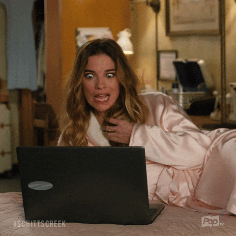 Schitt's Creek gif. Annie Murphy as Alexis lounges in a robe on a bed in front of an open laptop. She looks at the laptop, her eyes widening comically, twists her hair in her hand and says what appears as text, "Yum!"
