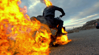 Movie gif. Nicholas Cage as Ghost Rider in Ghost Rider. He's jetting away on his motorbike and flames, gravel, and smoke whip behind him.