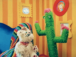 TV gif. A cactus puppet with pink flowers talks to Scruffy, a white fluffy dog puppet in Happy Place, wearing a tiny cowboy hat, saying, "Well, thank you!" on a brightly-colored cartoon-style living room set.