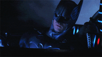 Movie gif. Batman looks at us while driving Batmobile, gives a thumbs up, and zooms forward.