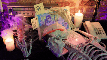 Video gif. Skeleton lays facedown at a desk, gripping the top of a busy-looking laptop screen, surrounded by spooky candles and lightning flashes.