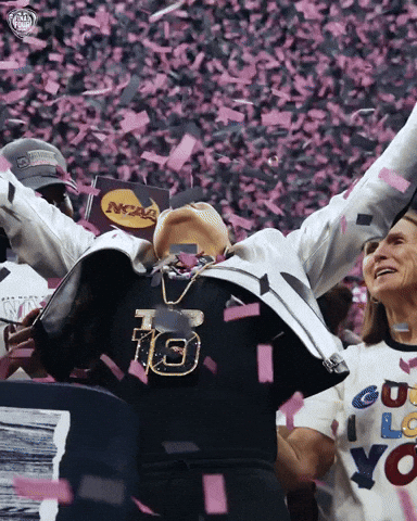 Sports gif. Dawn Staley, head coach of the South Carolina Gamecocks, raises her arms and leans back in celebration as pink and black confetti falls around her in slow motion.