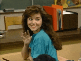 TV gif. Tiffani Thiessen as Kelly in Saved by the Bell looks over her shoulder and gives a flirtatious finger wave.