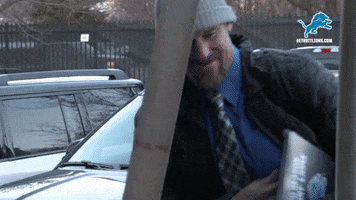 Sports gif. Dan Campbell, head coach of the Detroit Lions, is walking into the stadium and he gives us multiple fist pumps as he hollers. He's dressed in cold weather gear and steam comes out of his mouth, indicating how cold it is.