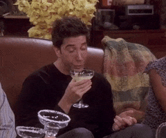 Friends gif. David Schwimmer as Ross appears drunk, with half-closed eyes, as he takes a sip from a margarita.