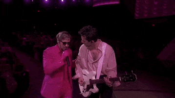 Oscars 2024 GIF. Ryan Gosling walks up slowly on stage with Mark Ronson, who is playing the guitar and he's performing I'm Just Ken. The two men look at each other and Gosling gently knuckles Ronson's face, in an endearing, understanding manner that being a man is hard. Ronson spins away and Gosling continues singing while trying not to laugh.