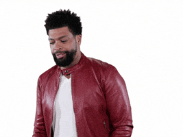 Celebrity gif. Wearing a dark red leather jacket, comedian Deray Davis sways in front of a pure white backdrop with a soft smile across his face. Right when he looks at us, he jolts back and screams in fear.