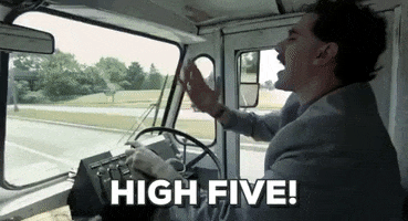 Movie gif. Driving on a highway in a truck with its steering wheel on the left, Sacha Baron Cohen as Borat gives a high five to someone in the seat next to him. He then looks at his palm as if the person next to him has wet hands. Text, "High five!"