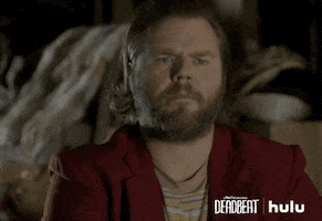 TV gif. Tyler Labine as Kevin in Deadbeat. He looks at something inquisitively and puts a hand to his mouth as he ponders.