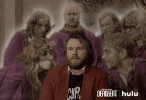 TV gif. Tyler Labine as Pac on Deadbeat squirms uncomfortably as a crowd of ghosts encircle him. They all nod along with one in the front that speaks at Pac earnestly. 