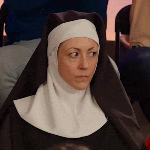 Video gif. A Nun sits in an audience and looks over, side eyeing someone while shaking her head. She has an unamused look on her face.